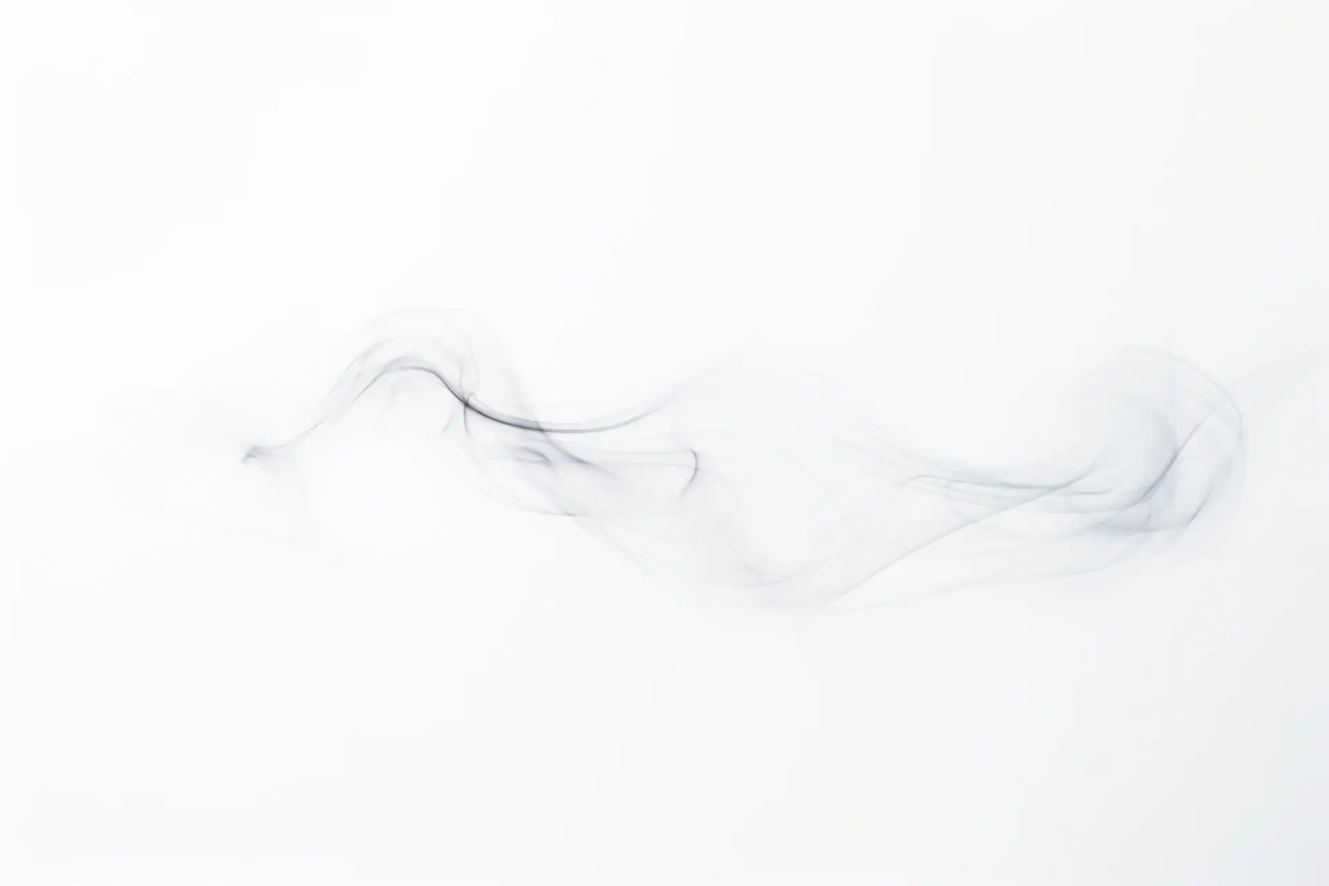 Fine dark smoke in perpetual flux against white — a shape without a fixed core